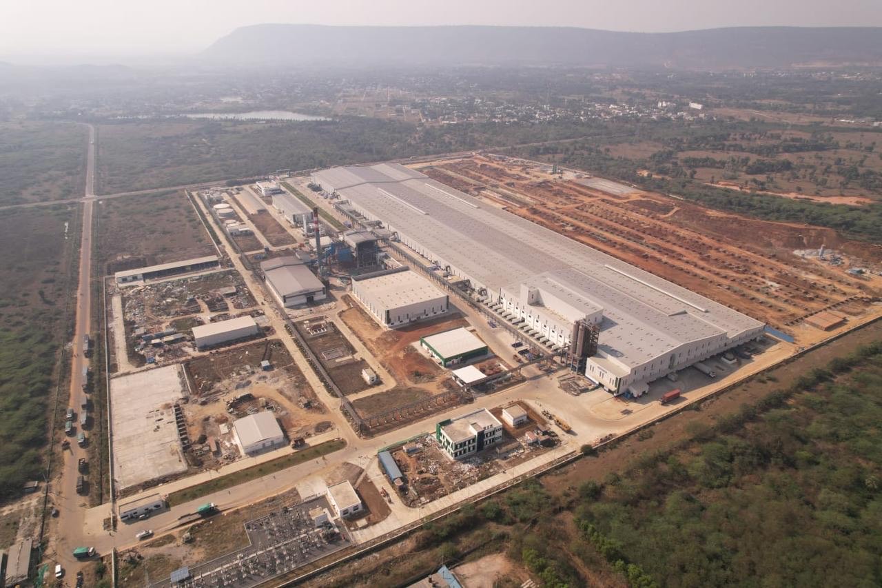Aerial view of a greenfield tire plant under construction: main production halls roofed, utilities and substation going in, and the expansion area cleared alongside