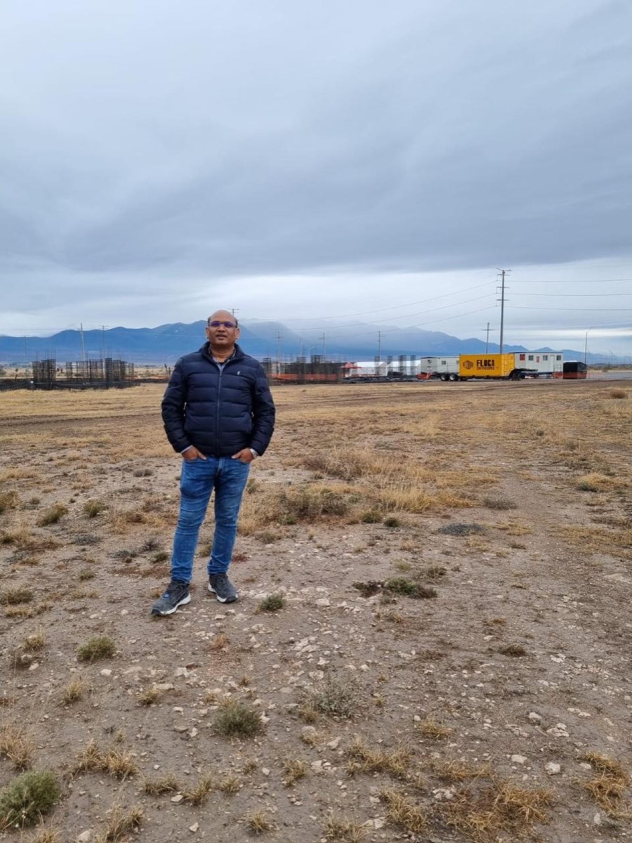 Pradeep Kumar Agarwal standing on the bare project site, with reinforcement cages and site offices in the distance